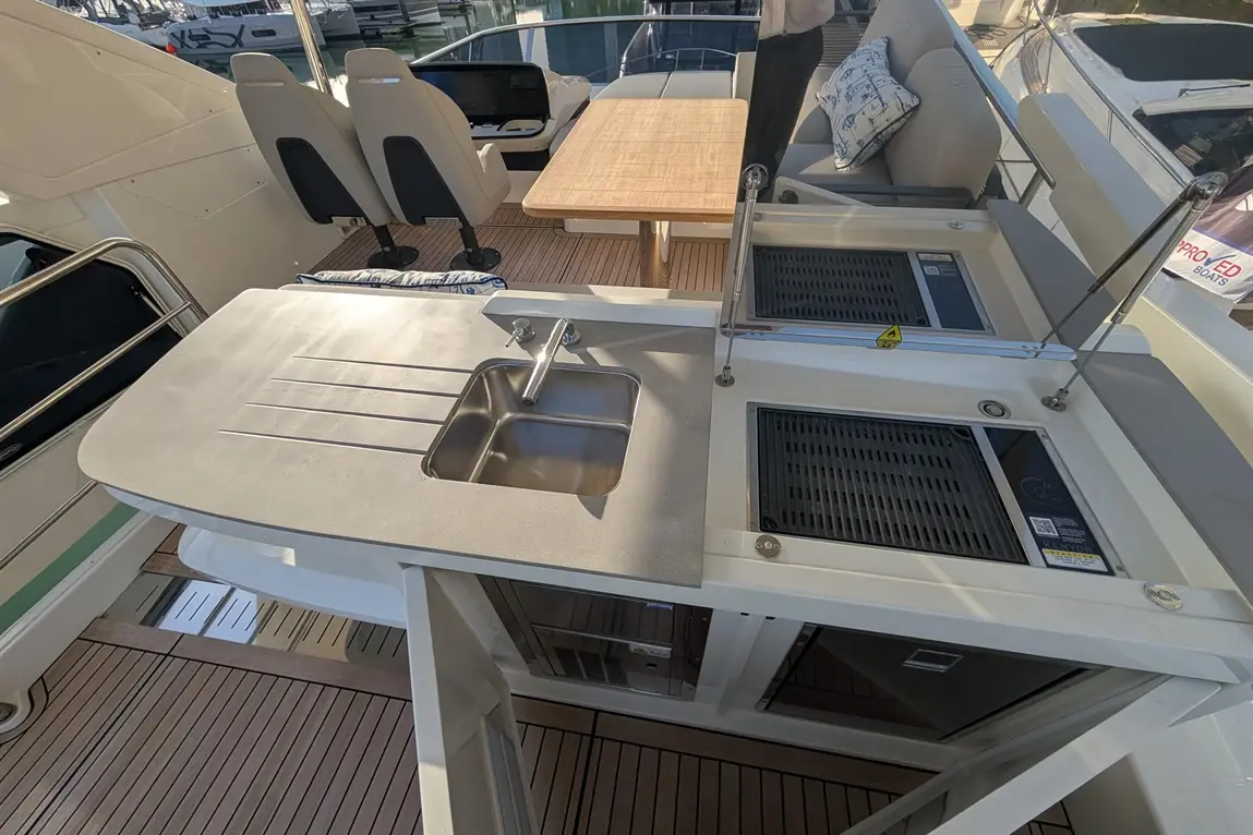 Modern boat deck featuring a sink, cooking area, and seating, with a wooden table and sleek interior design.